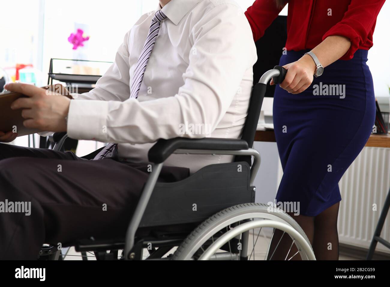 Frau trägt Mann im Anzug am Rollstuhlarbeitsplatz Stockfoto