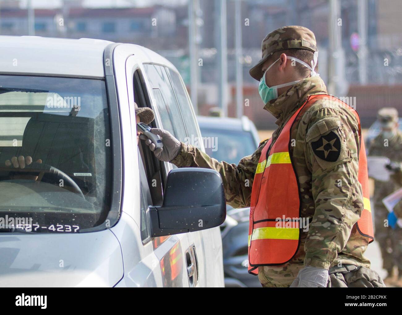 Ein US-Soldat beatmelt Passagiere für COVID-19 mit einem Thermometer an einem Eingangstor für Army Garrison Humphreys, 27. Februar 2020 in Pyeongtaek, Südkorea. Der Ausbruch des neuartigen Coronavirus in Südkorea ist an zweiter Stelle nur für China. Stockfoto