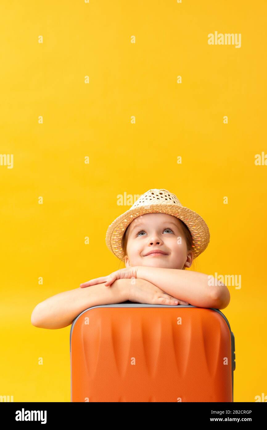 Abenteuer-Reise-Konzept. Portrait eines süßen verträumten kleinen Mädchens mit Koffer. Nahaufnahme von Kindern auf gelbem Hintergrund im Studio. Kopierbereich. Stockfoto