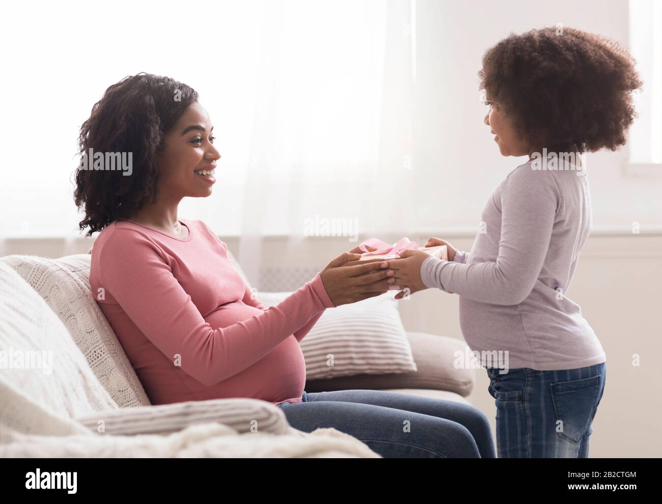 Schwangere Frau, Die Geschenkschachtel Von Ihrer Liebevollen Kleinen Tochter Afro Erhält Stockfoto