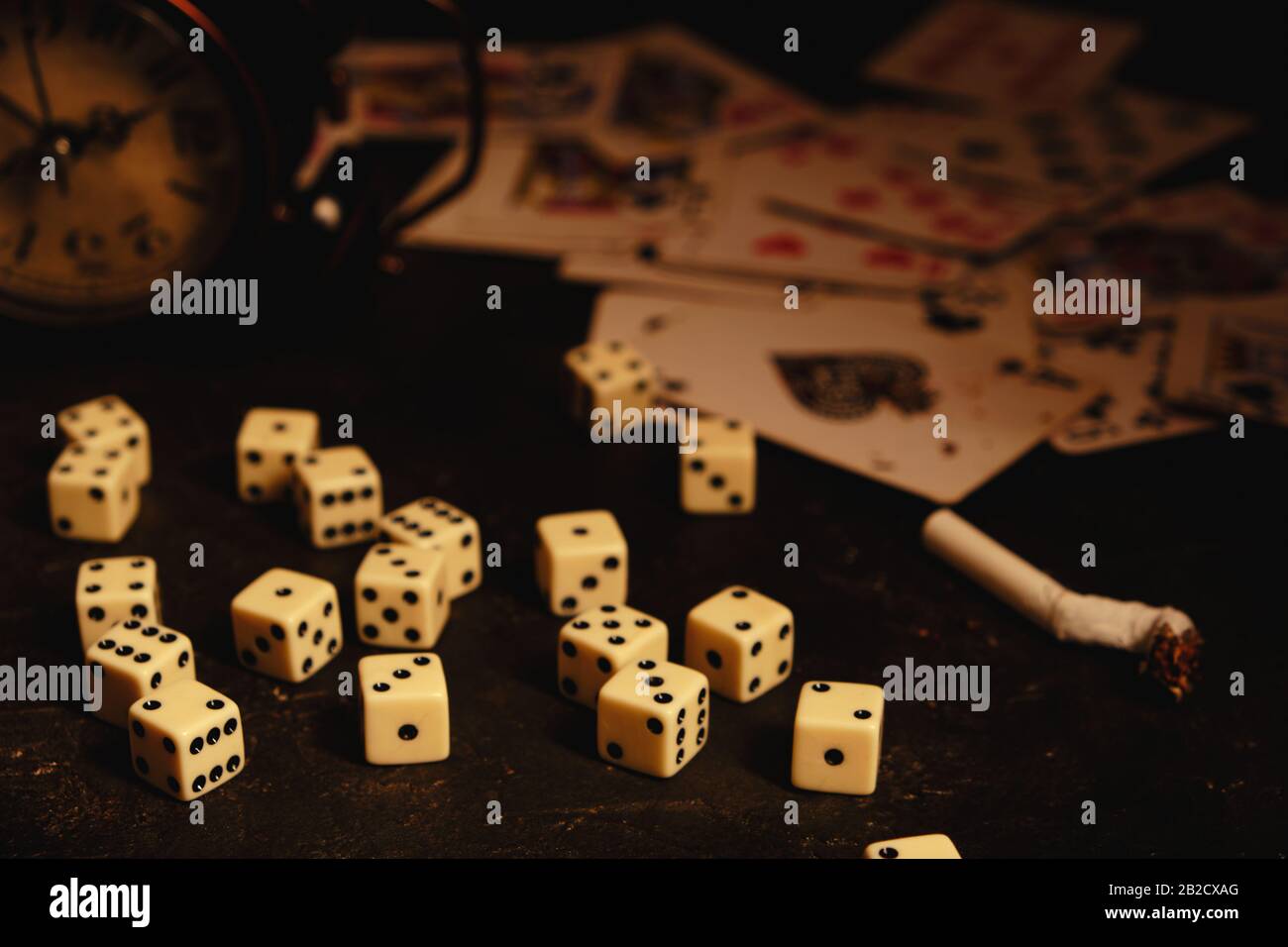 Würfel, Zigaretten, Karten und ein aufgegebener Wecker auf einem Tisch in einem Underground-Casino Stockfoto