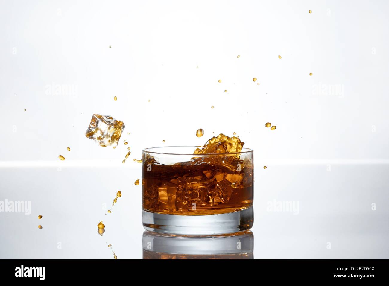 Ein Eiswürfel spritzt in ein Glas Whisky Stockfoto