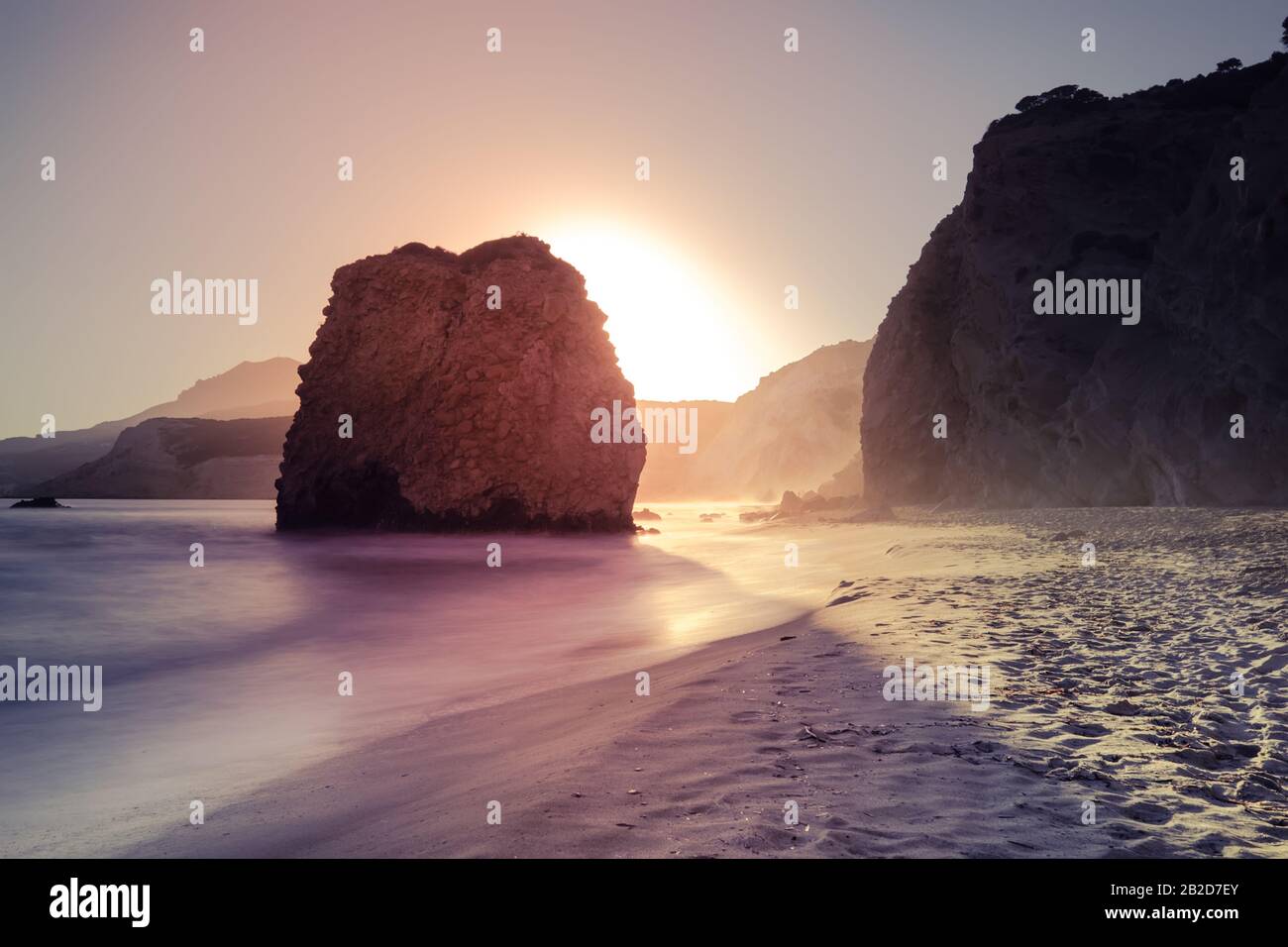 Fantastischer Sonnenuntergang auf der Insel Milos. Sandiger Strand und sanfte Meeresbrandung in der ägeischen Meere. Große Steinfelsen im Wasser. Ruhiger Abend mediterrane Landschaft auf den Kykladen I Stockfoto