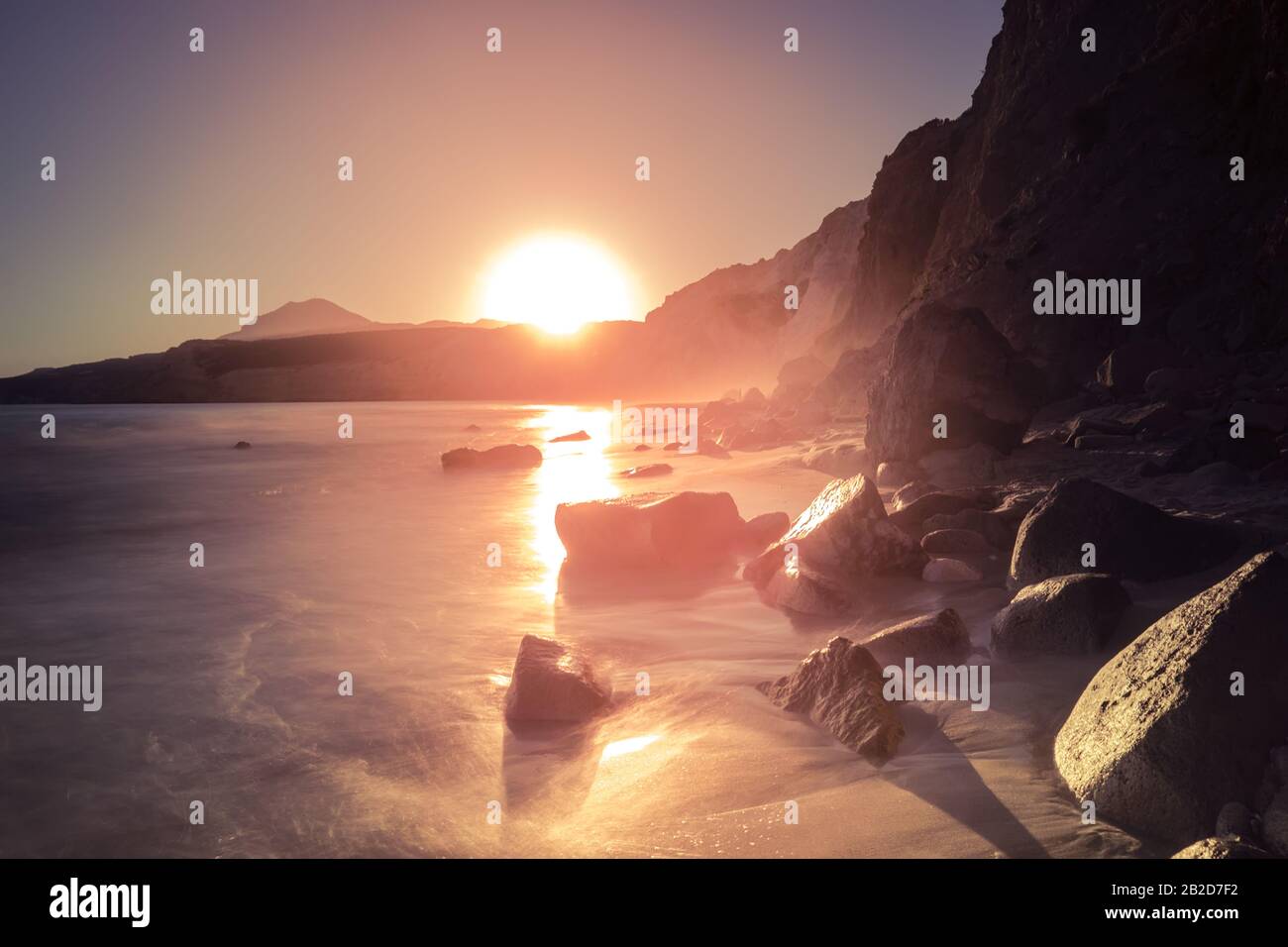 Fantastischer Sonnenuntergang auf der Insel Milos. Sandiger Strand und sanfte Meeresbrandung in der ägeischen Meere. Große Steinfelsen im Wasser. Ruhiger Abend mediterrane Landschaft auf den Kykladen I Stockfoto