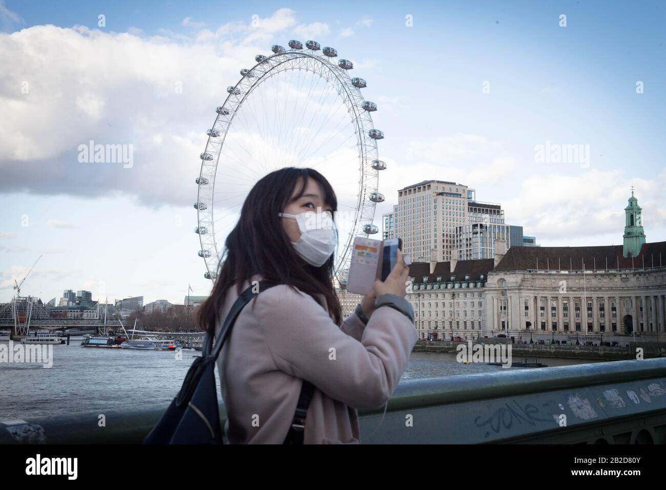 Eine Frau, die eine Gesichtsmaske trägt, nimmt von der Westminster Bridge in London ein Foto auf ihrem Telefon auf, da Shadow Health Secretary Jonathon Ashworth sagt, dass er die Schließung von Städten unterstützen würde, um die Ausbreitung von Coronavirus zu kontrollieren. PA Foto. Bilddatum: Montag, 2. März 2020. Ashworth sagte am Montag beim BBC-Frühstück, dass er Klarheit von der Regierung über die nächsten Schritte zur Eindämmung des Covid-19-Virus wünschte. Auf die Frage, ob er die Schließung von Städten unterstützen würde, um die Ausbreitung innerhalb des Vereinigten Königreichs zu verhindern, sagte Ashworth: "Wenn die medizinische Beratung und der wissenschaftliche Rat Maßnahmen in dieser Richtung ergreifen sollen, von c Stockfoto