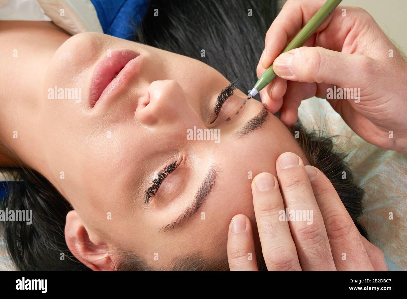 Plastischer Chirurg und junge Frau mit Korrekturlinien vor der kosmetischen Operation, die Linien auf die Augen zeichnen Stockfoto