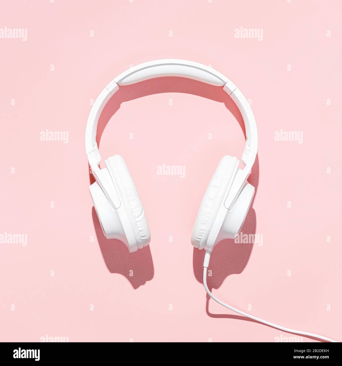 Flache, weiße Kopfhörer auf modernen blassrosa Tischtapeten. Freier Platz für kreatives Design von Text und Inhalt. Stockfoto