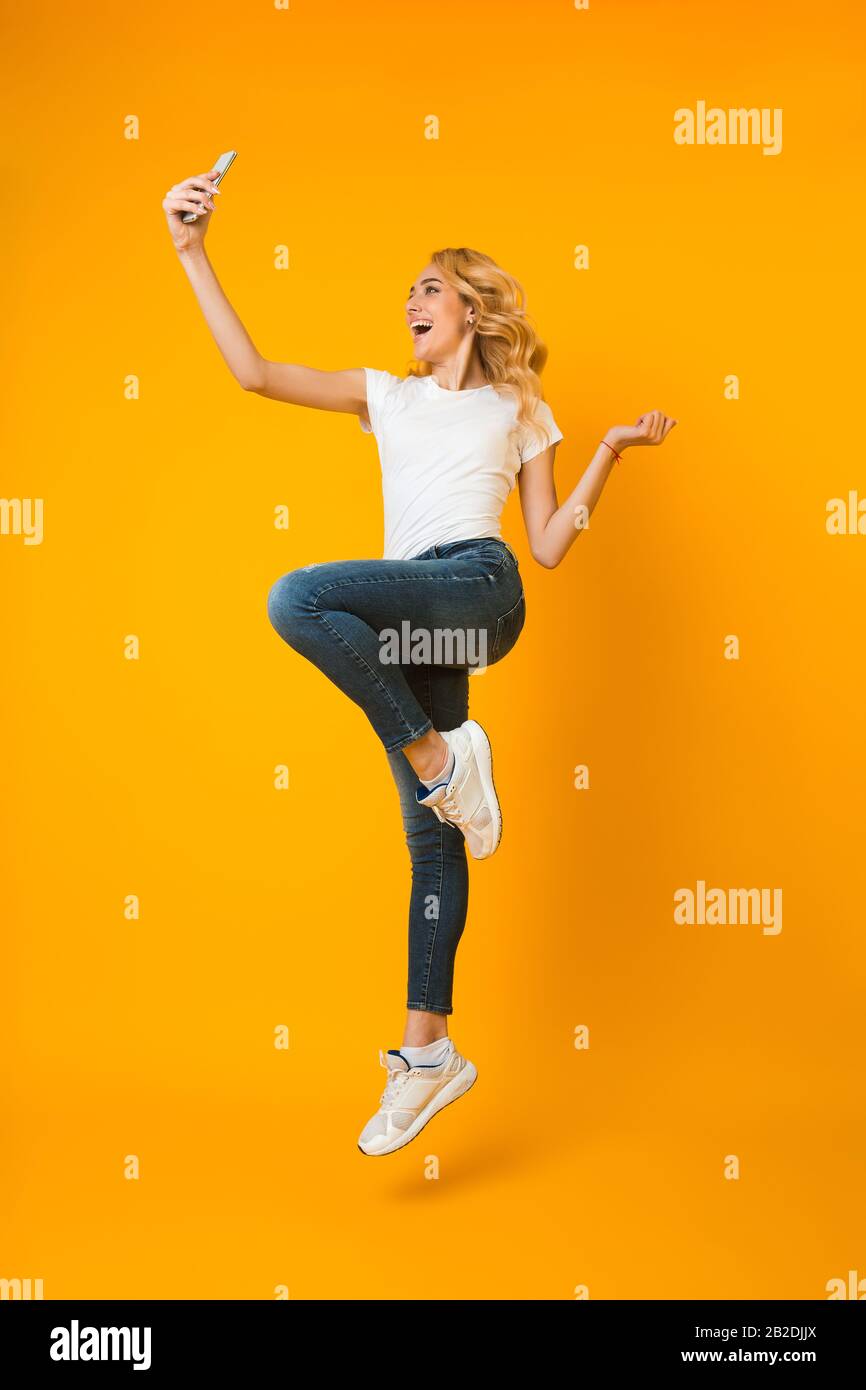 Überfreute Frau springt und nimmt selfie am Telefon mit Stockfoto