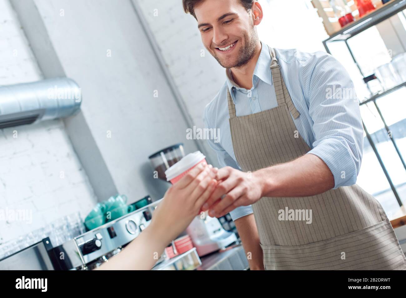 Kaffeepassion. Der junge Barista im Coffeeshop serviert dem Kunden eine Tasse heißen Kaffee und lacht fröhliche Nahaufnahme Stockfoto