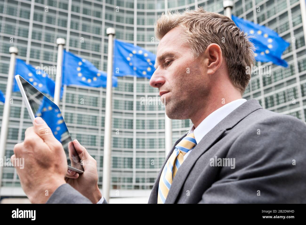 Ein ernsthafter europäischer Unternehmer, der Tablet-Computer draußen vor der Reihe von EU-Flaggen in Brüssel, Belgien, verwendet Stockfoto