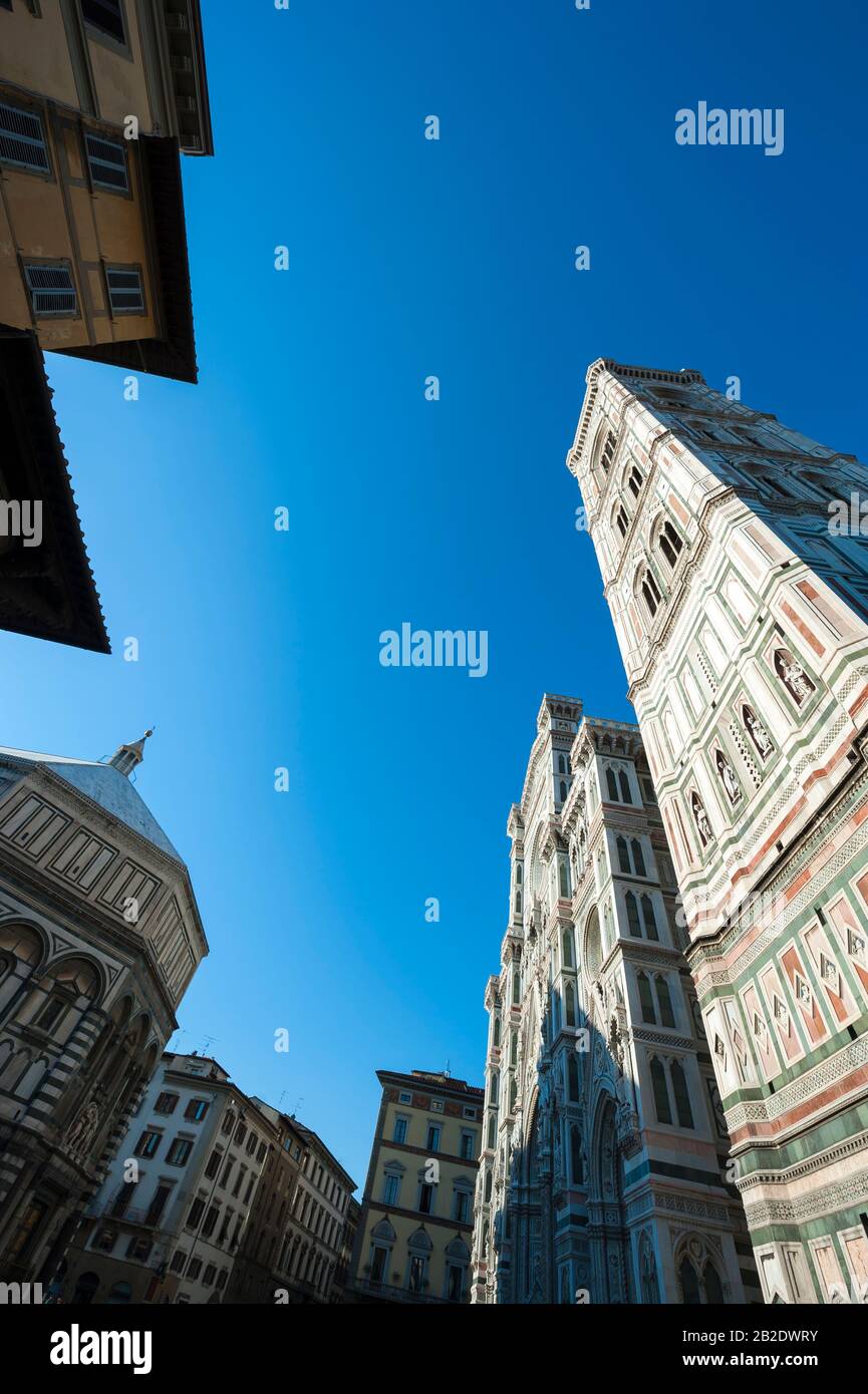 Dramatischer Chiaroscuro-Blick auf die Piazza del Duomo mit dem Portal und dem Turm der Kathedrale gegen den hellblauen Himmel in Florenz, Italien Stockfoto