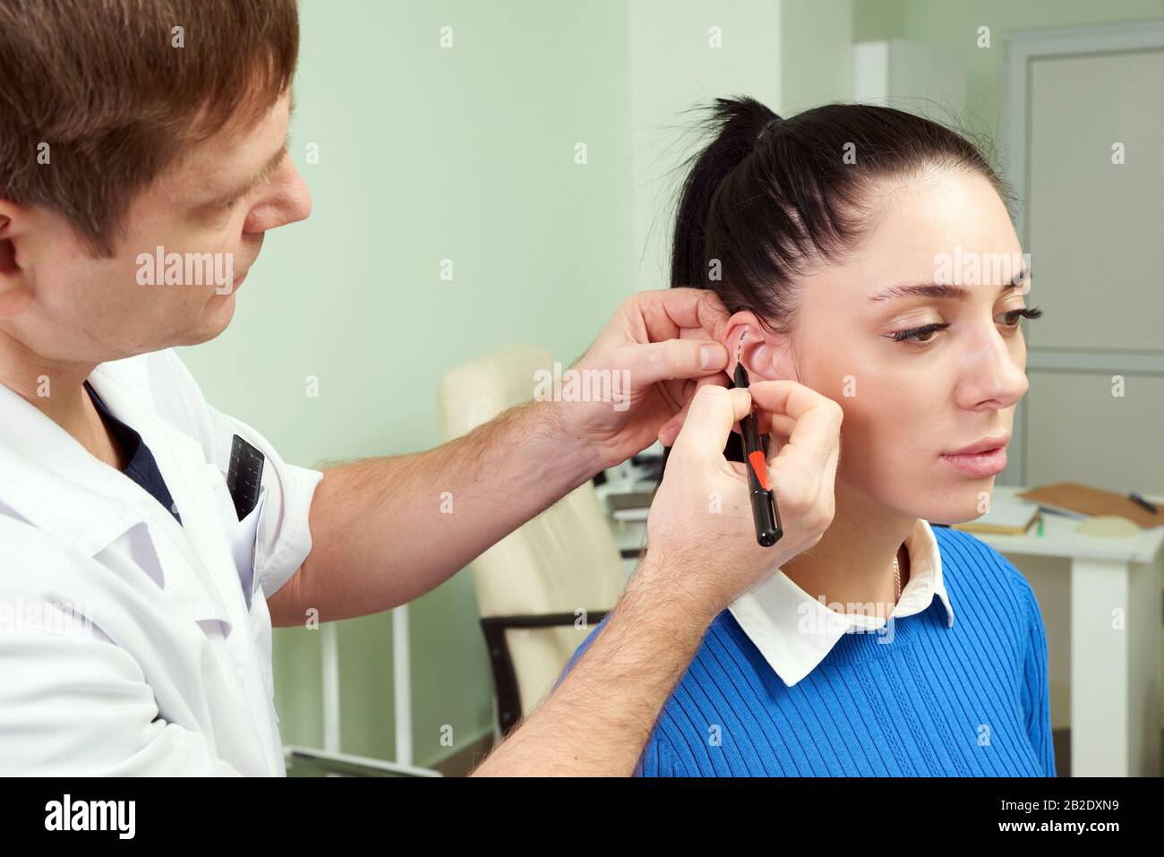 Der plastische Chirurg untersucht das Ohr des Patienten vor der plastischen Operation und der Zeichnung von Linien Stockfoto