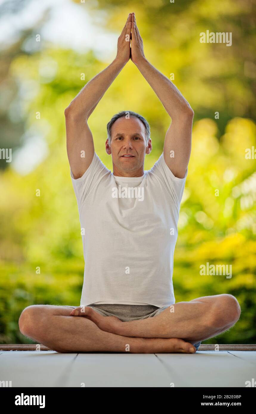 Porträt eines glücklichen Mannes mittleren Alters, der Yoga auf einem Deck praktiziert Stockfoto