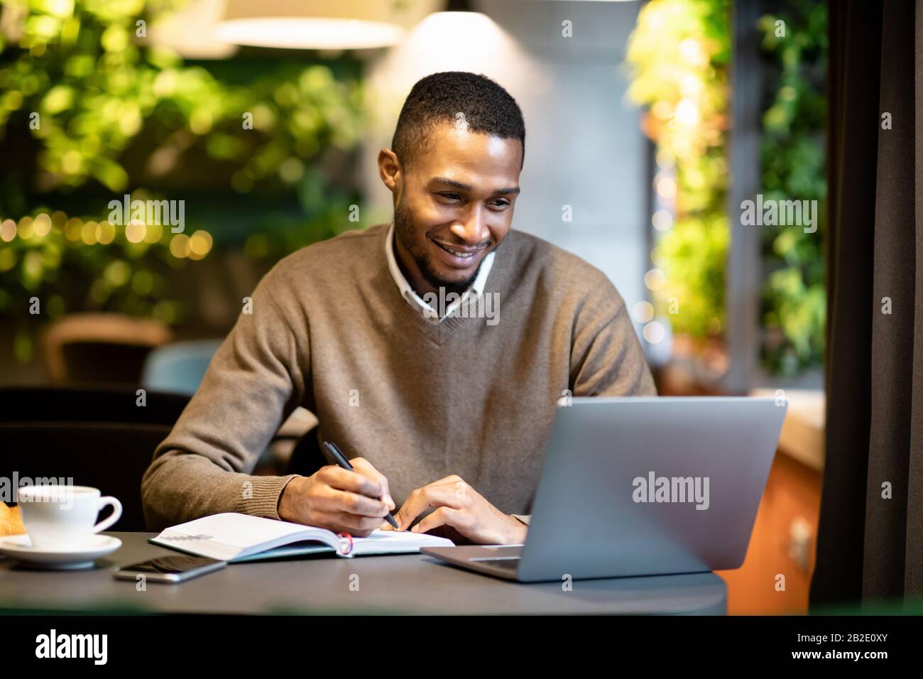 Black Business Guy, der sich Notizen im Notebook mit Tablet gemacht hat Stockfoto