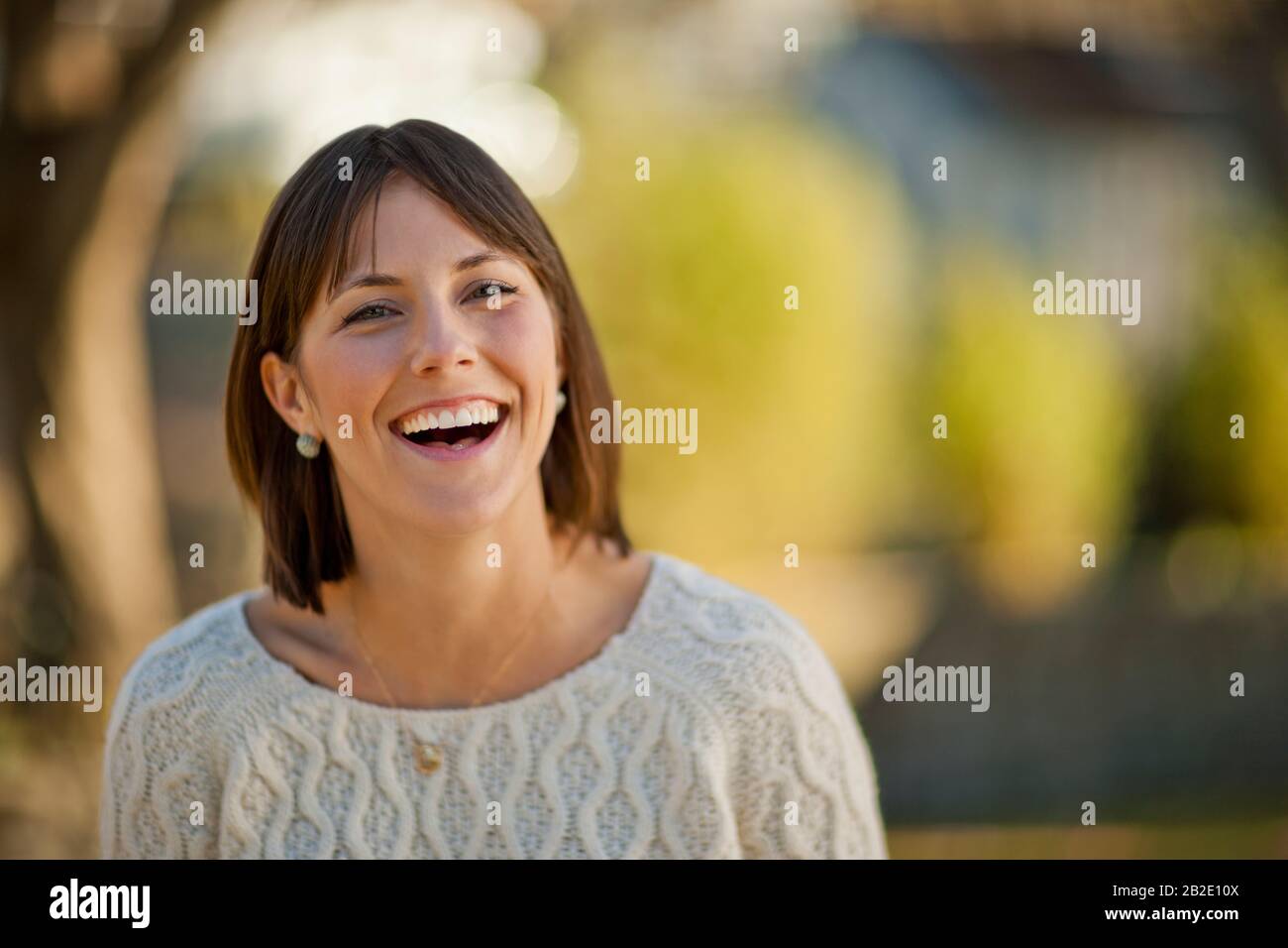 Porträt einer lächelnden jungen Frau, die sich in einem sonnigen Park entspannen kann Stockfoto