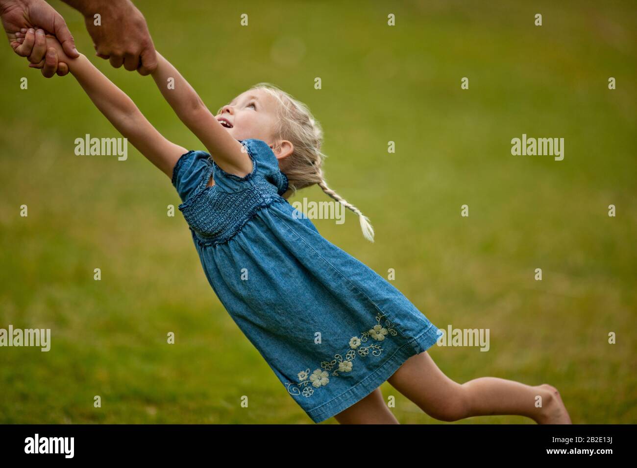 Glückliches kleines Mädchen, das Spaß hat, während ihr Vater sie auf dem Rasen herumschaukelt Stockfoto