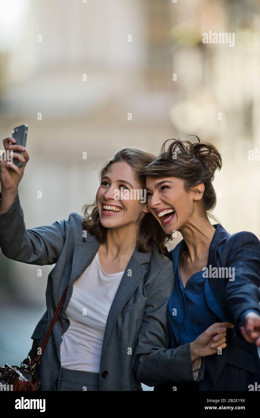 Zwei lächelnde junge Frauen, die gemeinsam ein selfie auf einer Straße in der Stadt nehmen Stockfoto