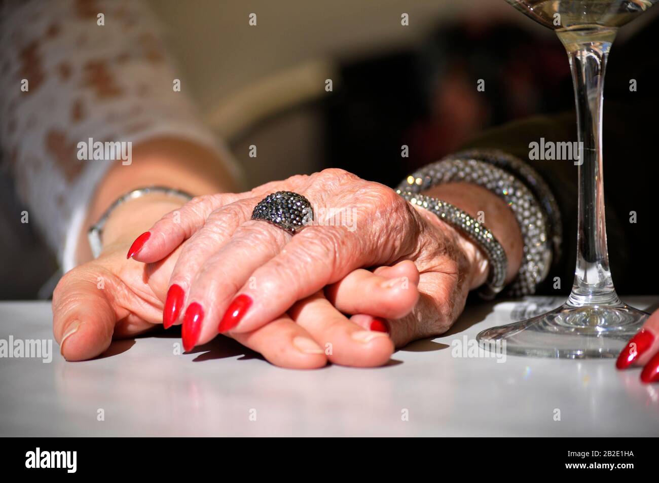 Ältere Mutter hält die Hand der Tochter auf einem Restauranttisch mit einem Glas Weißwein daneben. Tageszeitteilungmit der Mutter. Hände halten Stockfoto