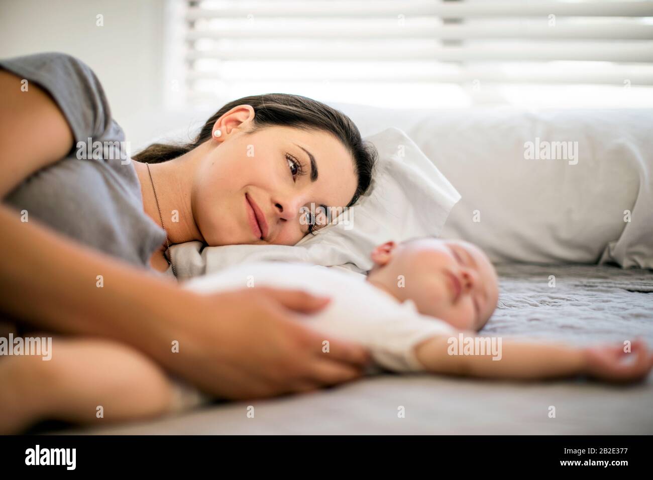 Die Mutter, die sich im mittleren Alter mit ihrem schlafenden Mädchen auflegt Stockfoto