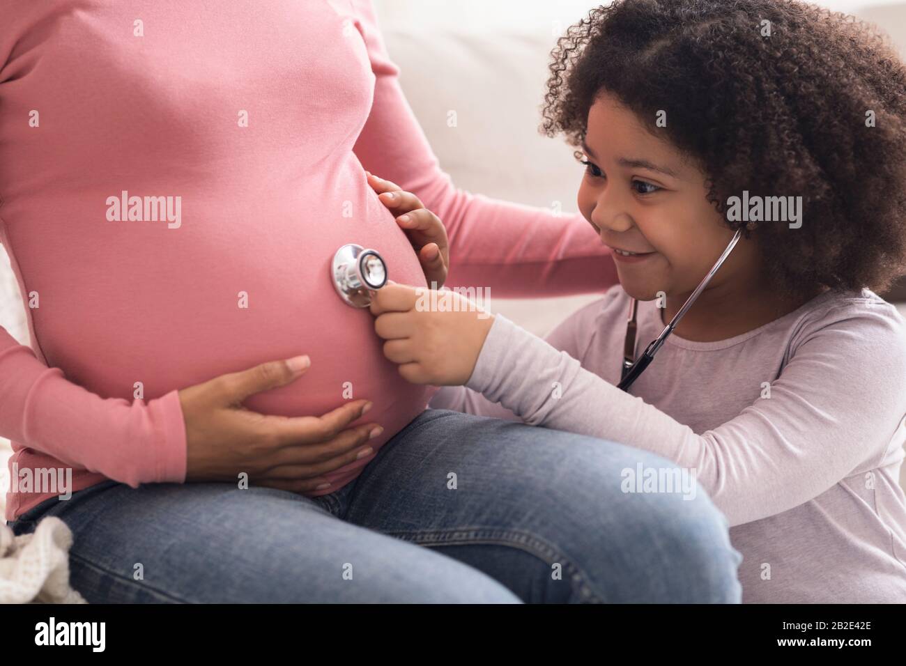Überglücklich, Afro Girl Mit Stethoskop Den Schwangeren Bauch Ihrer Mutter Hört Stockfoto