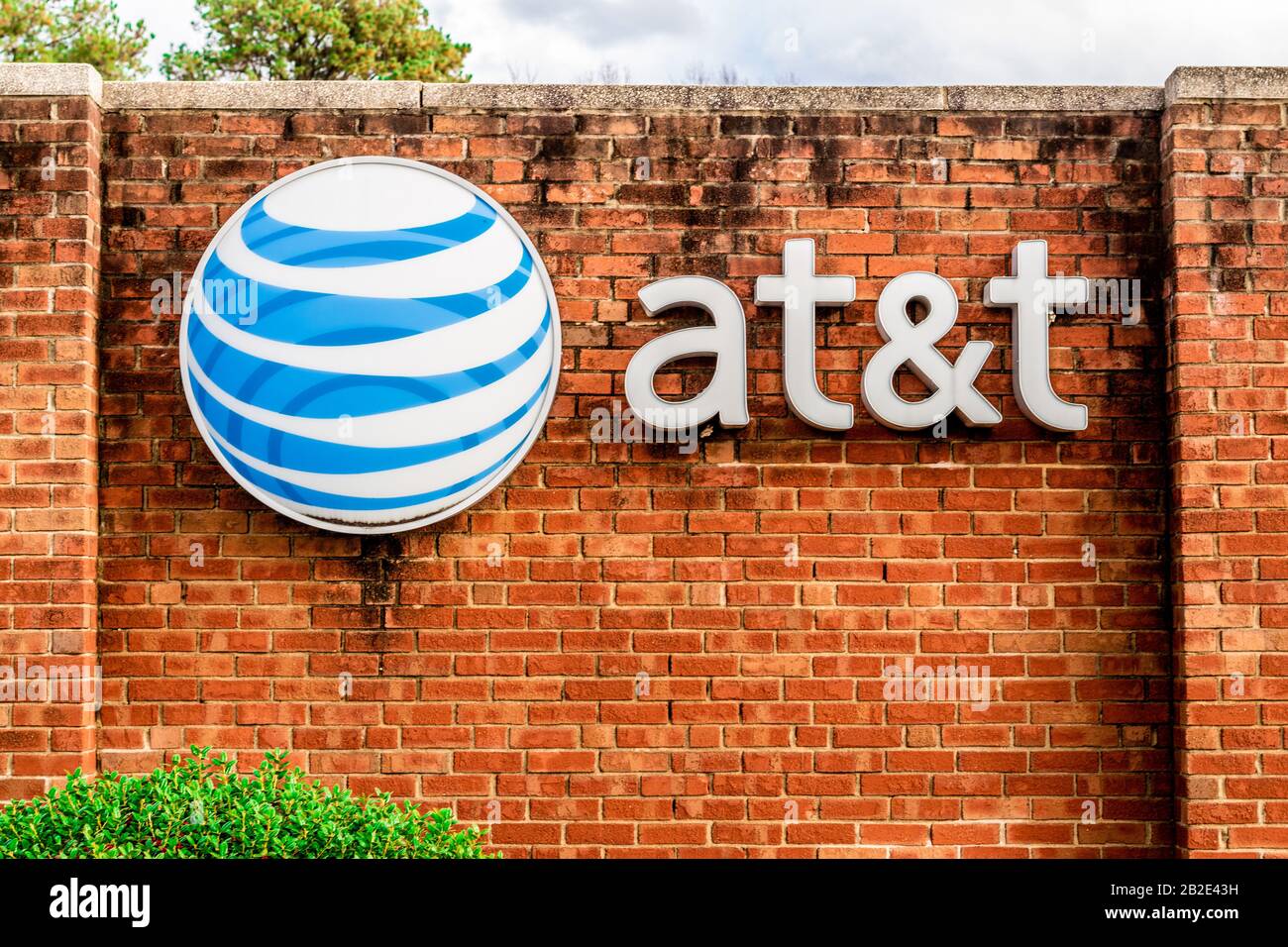 Charlotte, NC/USA - 14. Dezember 2019: Mittlerer horizontaler Schuss von Marke "AT&T" und Logo auf einer roten Ziegelwand mit Bäumen, geparkten Autos und Sturm c Stockfoto