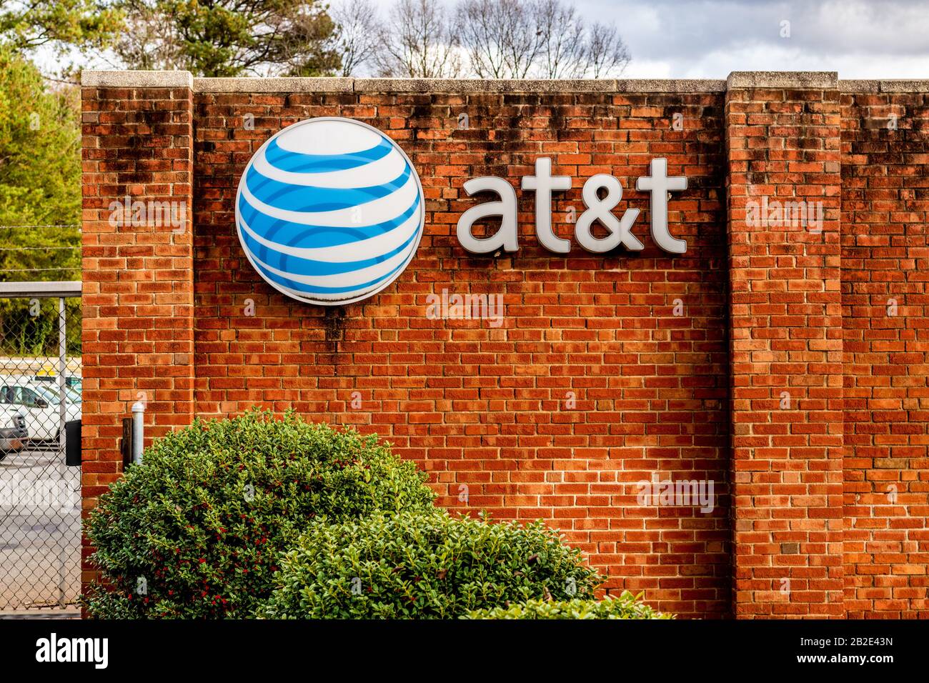 Charlotte, NC/USA - 14. Dezember 2019: Mittlerer horizontaler Schuss von Marke "AT&T" und Logo auf einer roten Ziegelwand mit Bäumen, geparkten Autos und Sturm c Stockfoto