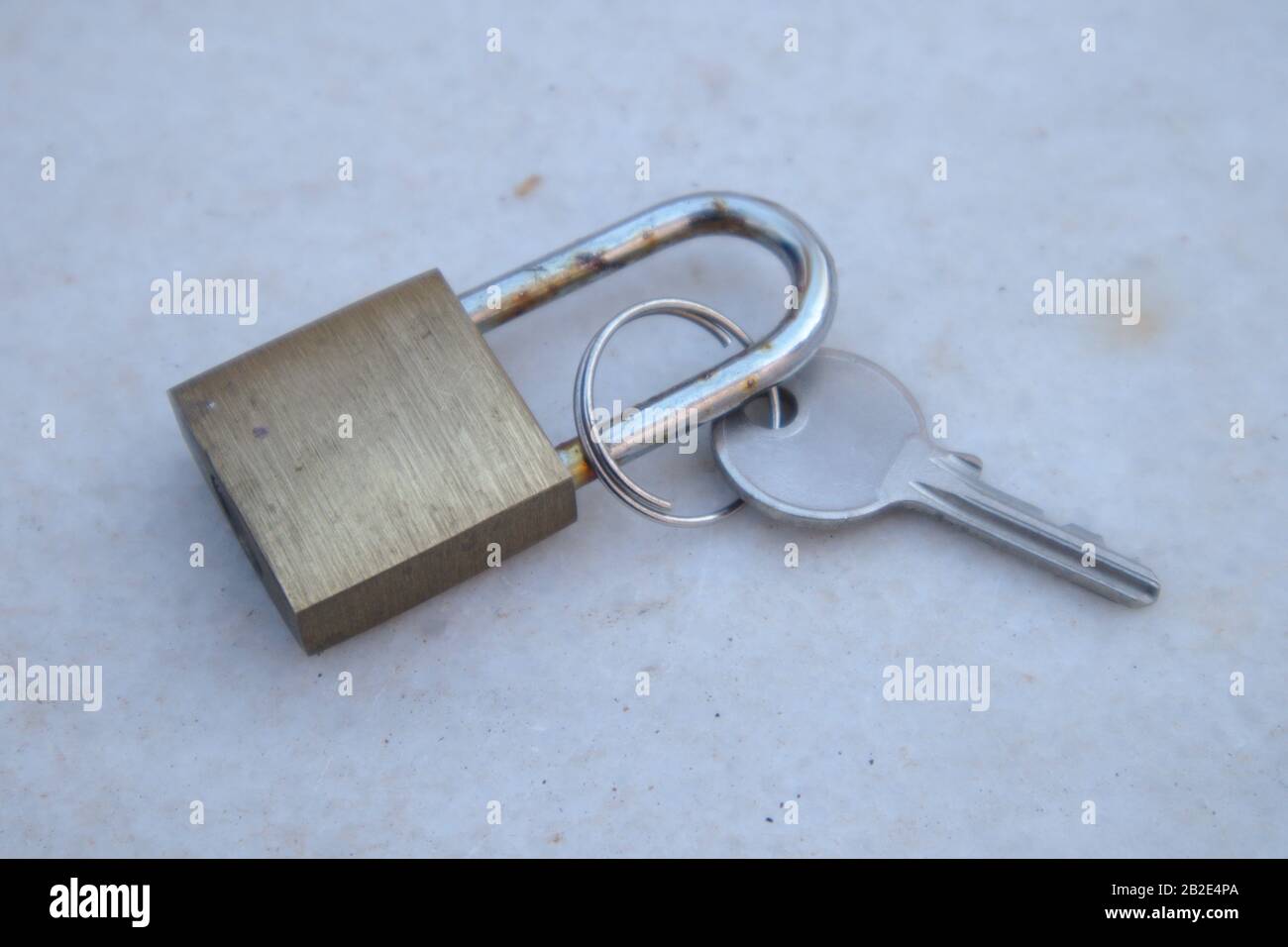 Nahaufnahme eines Vorhängeschlocks neben dem Schlüssel, der ihn auf einer verwitterten Oberfläche aus grauem Marmor öffnet Stockfoto