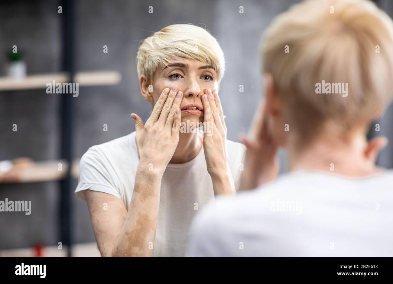 Müde Mittelalte Frau, Die Das Gesicht Berührt, Das Im Spiegel Im Badezimmer Aussieht Stockfoto