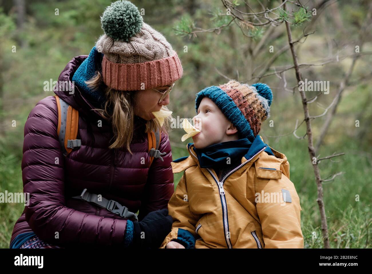 Mutter und ihr Sohn machen dumme Gesichter beim Essen und Wandern im Winter Stockfoto