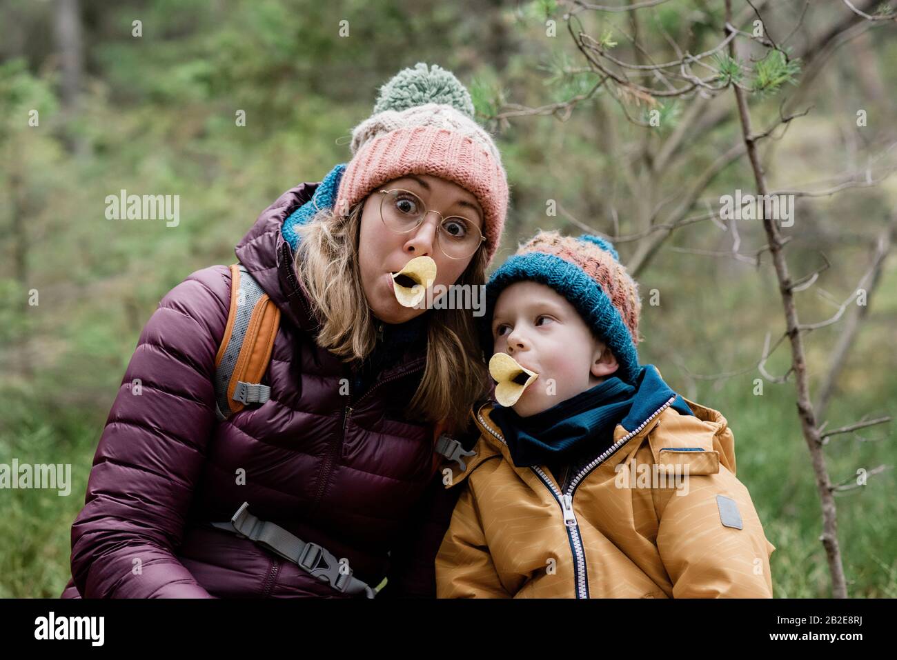 Mutter und Sohn machen dumme Gesichter mit Essen während der Wanderung im Winter Stockfoto