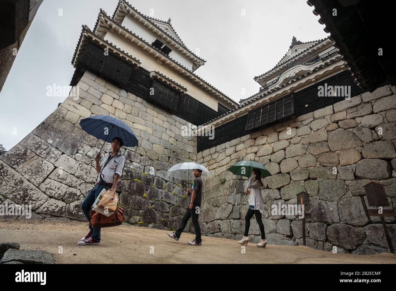 Touristen nutzen Regenschirme, wenn sie Matsuyama Castle, Matsuyama, Eihime, Japan erkunden. Stockfoto
