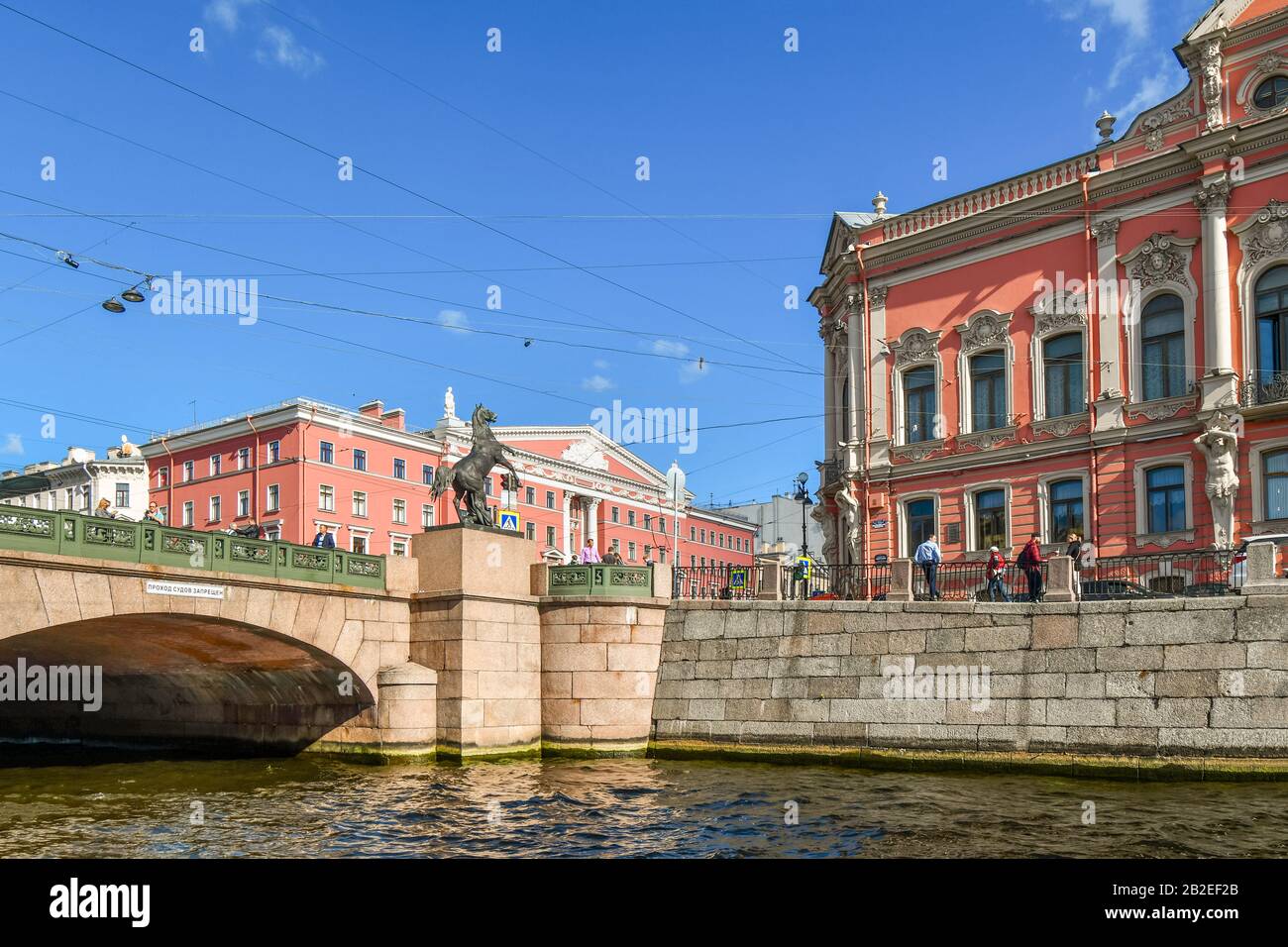 Blick von einem Kanal mit elektrischen und Telefonkabeln über die Anichkow-Brücke und die Pferdetamer-Skulptur in Sankt Petersburg, Russland. Stockfoto