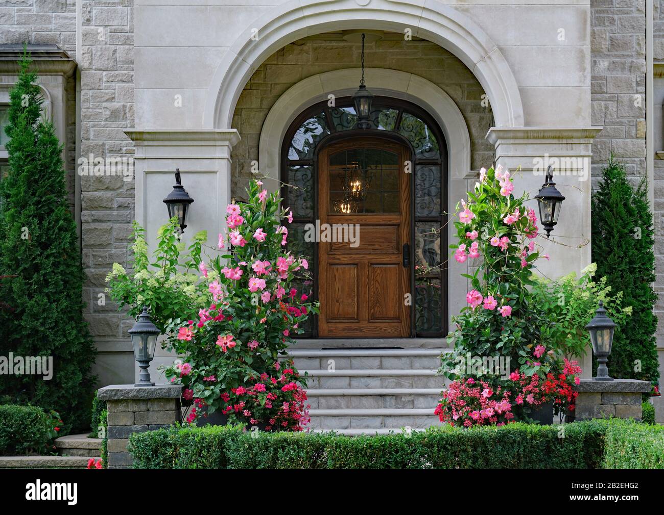 Eingangstür des eleganten Hauses mit steinernem Vorderteil und großen, stehenden Blumen aus Amaryllis Stockfoto