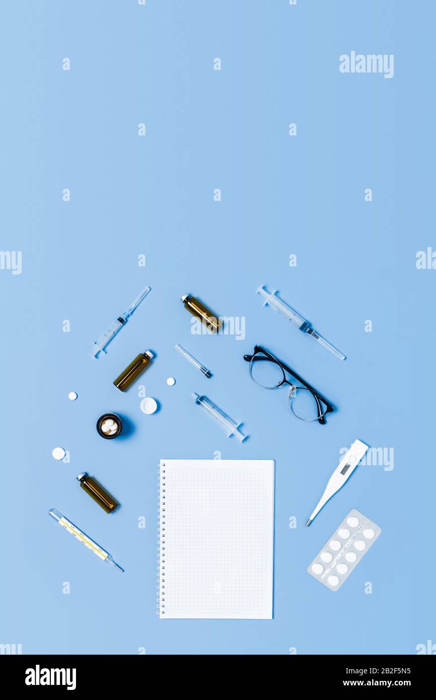 Medizinischer blauer Hintergrund mit unterschiedlichem Zubehör: Stethoskop, Thermometer, Spritze, Tablette und Notizblock. Vertikales Bild. Stockfoto
