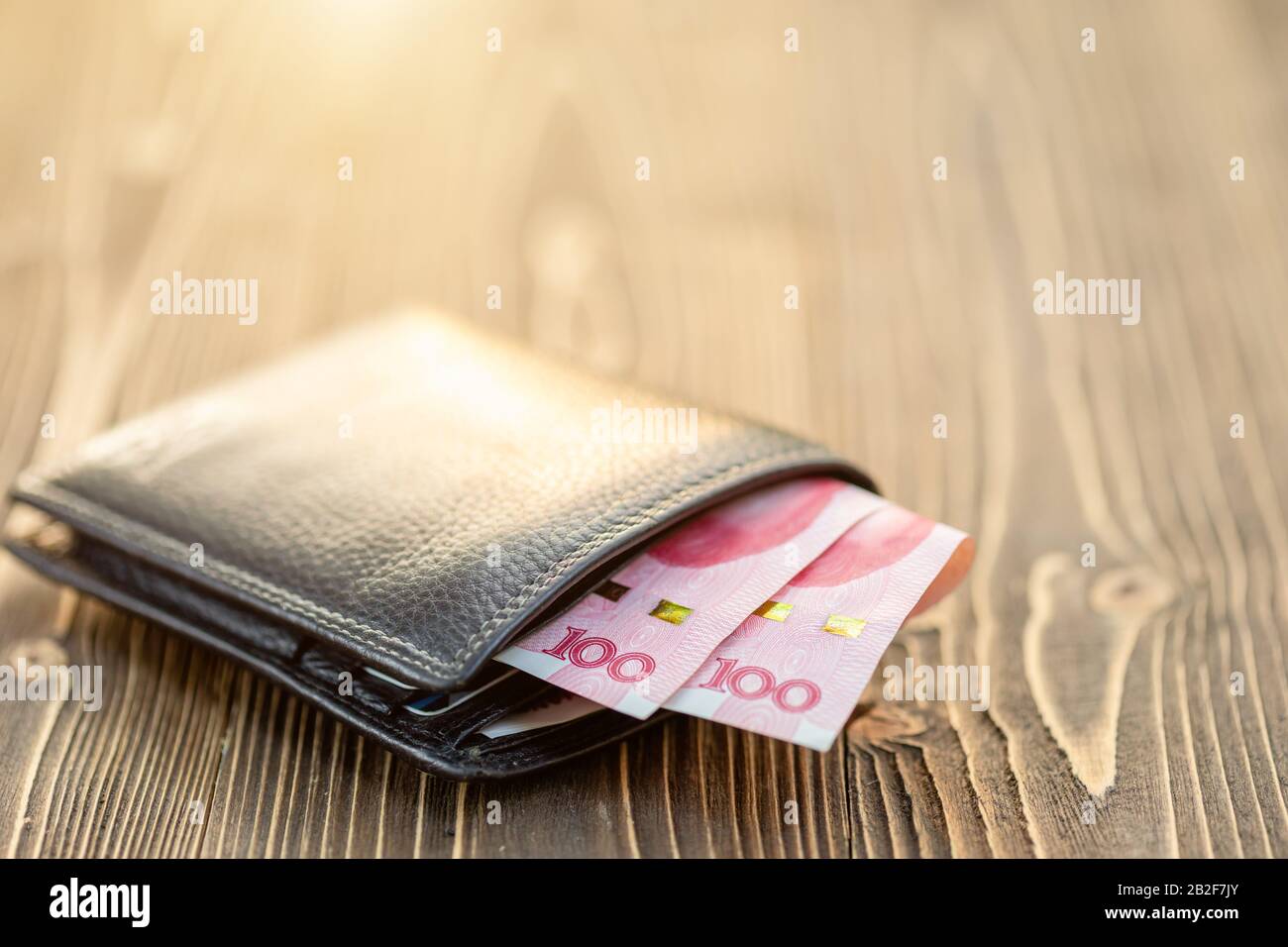 Nahaufnahme der schwarzen Ledertasche mit chinesischer Banknote auf Holztisch Stockfoto