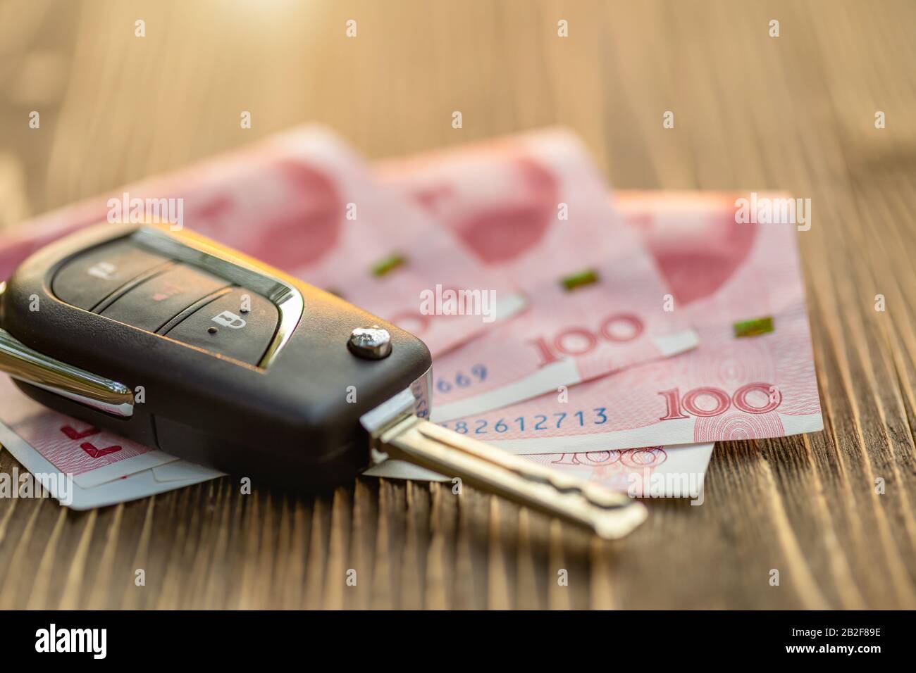 Schließen Sie neue Autoschlüssel mit chinesischer Banknote auf Holztisch. Autokauf oder Mietwagenkonzept Stockfoto