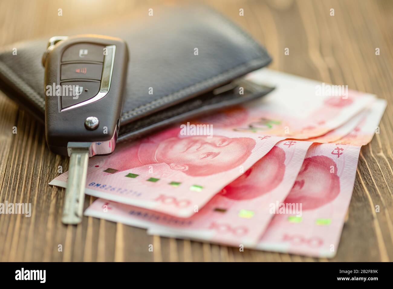 Schließen Sie neue Autoschlüssel mit chinesischer Banknote auf Holztisch. Autokauf oder Mietwagenkonzept Stockfoto