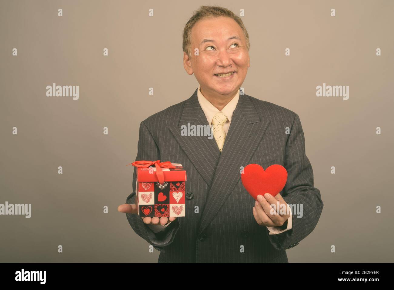 Studio mit einem Foto eines reifen asiatischen Geschäftsmannes, der vor grauem Hintergrund zum Valentinstag bereit ist Stockfoto