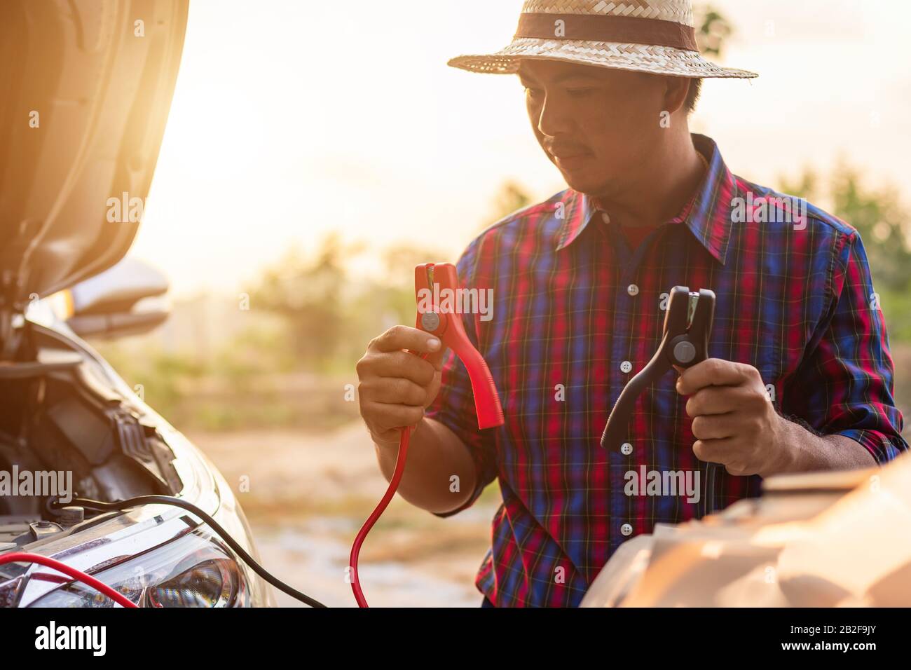 Asian man hält schwarz-rotes Batteriekabel und versucht, das Kabel mit seinem Auto zu verbinden. Fahrzeugwartung vor dem Fahrkonzept Stockfoto