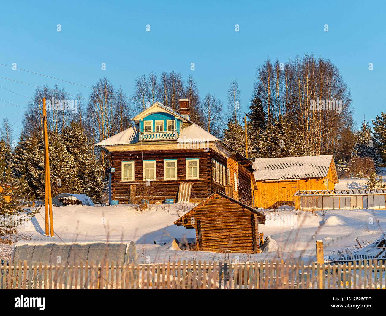 Winterblick auf Holzhaus im Dorf im russischen Norden. Altes schwarzes Haus auf dem Land in wunderschöner Sonneneinstrahlung gegen einen blauen Himmel. Kaltes Wetter Stockfoto