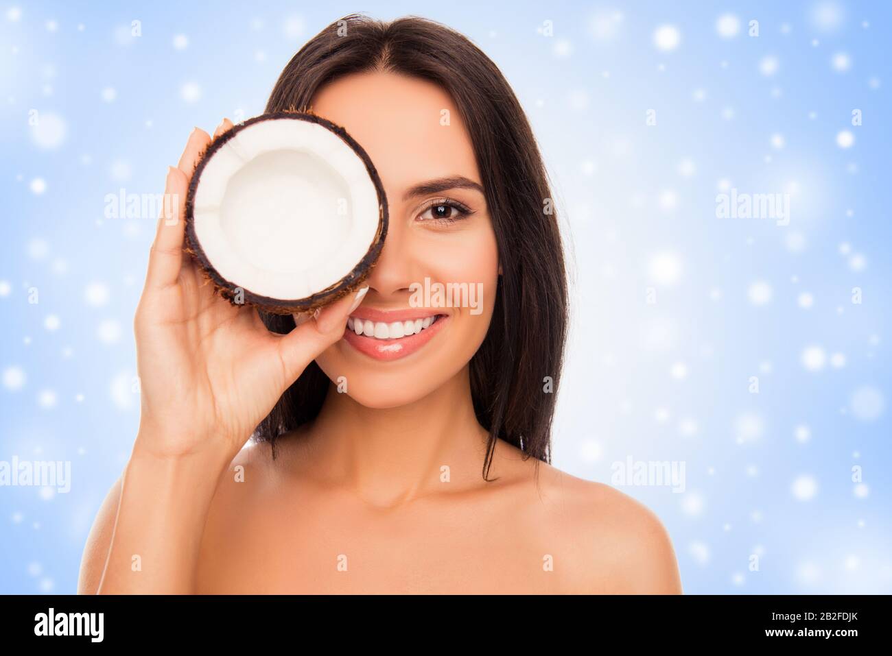 Fröhliche hübsche junge Frau holdind Kokosnuss mit Schnee bedeckt Stockfoto