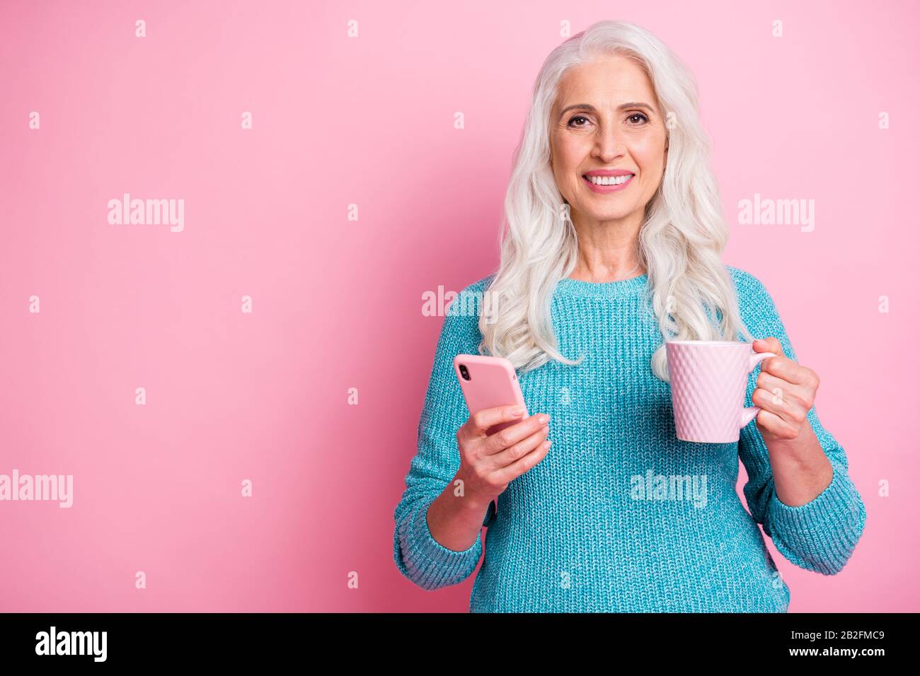 Charmante alte Frau moderne Kindermädchen verwenden Smartphone Textschreiben Schreiben Chat Familie Lesen soziale Netzwerk Nachrichten halten Getränkebecher tragen Casual Style Blau Stockfoto