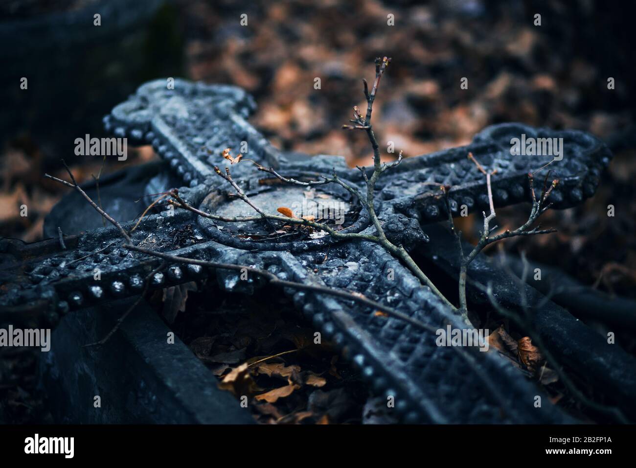 Auf dem Grab ist ein schönes altes Steinkreuz mit Muster gelegt, auf dem die gebogenen Äste von Bäumen und abgefallenen trockenen Blättern liegen. Der Herbst ist das Perso Stockfoto