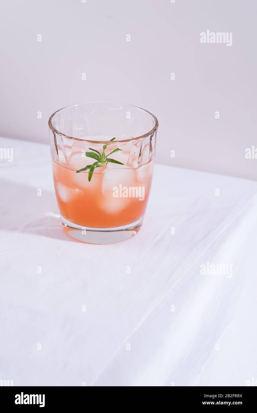 Rosa Cocktail mit Rosmarin und Eis aus Glas auf einem weißen Tischtuch auf dem Tisch Stockfoto