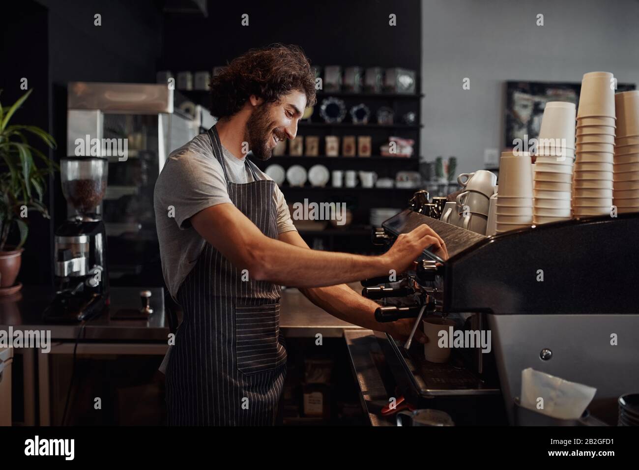 Lächelnder Mann mit Schürze, der Kaffee für den Kunden in seinem kleinen Unternehmen vorbereitet Stockfoto