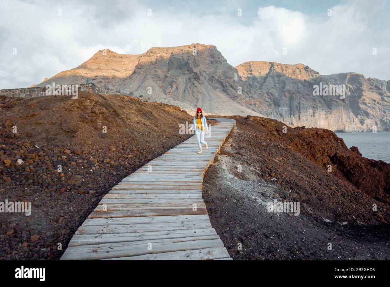 Frau, die auf dem malerischen Holzweg durch das felsige Land mit Bergen auf dem Hintergrund spazieren geht. Reisen auf dem nordwest-kap der Insel Tenera, Spanien Stockfoto