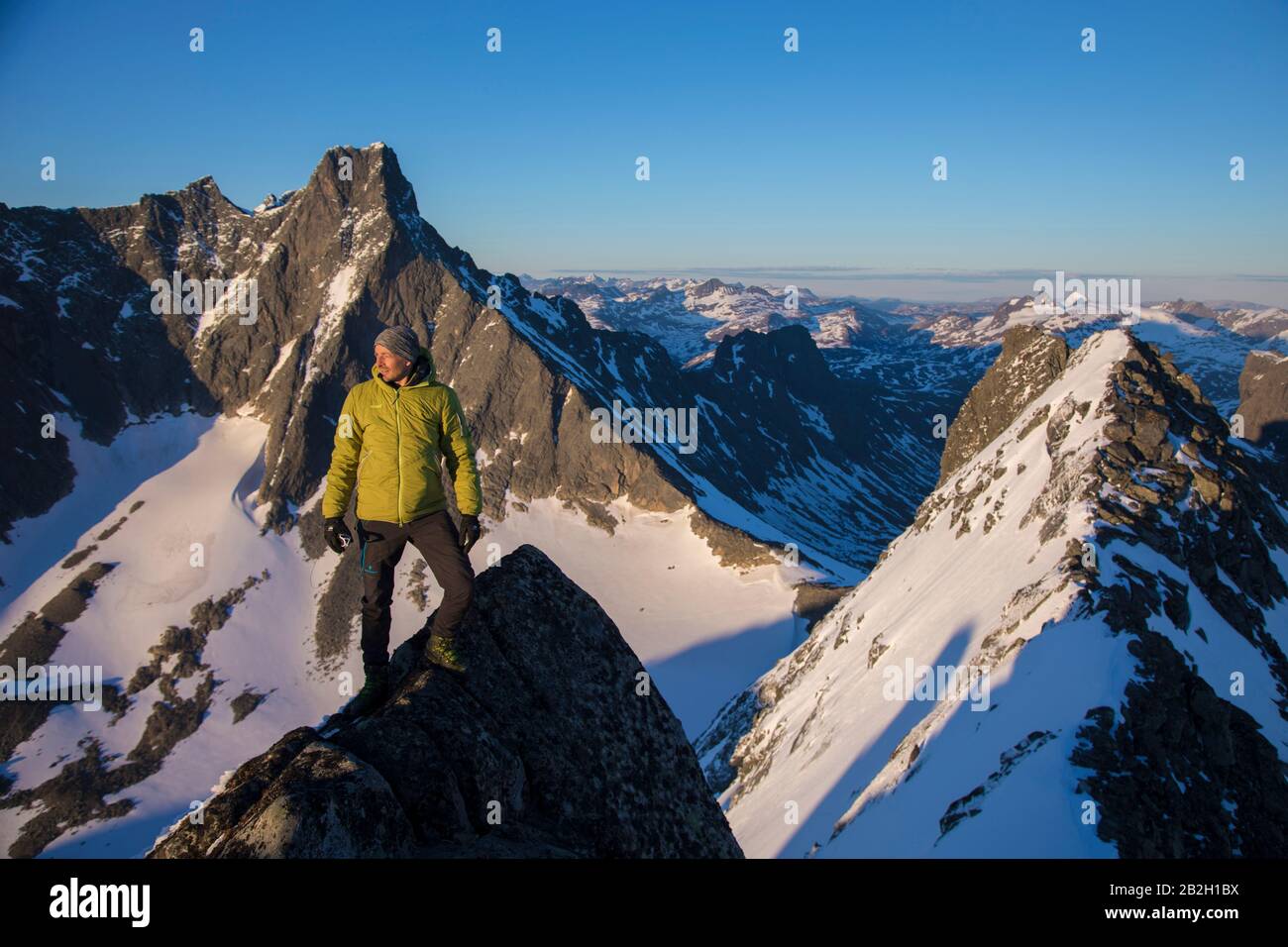 Mann steht auf der Weltspitze, auf dem Gipfel und blickt in die Berge Stockfoto