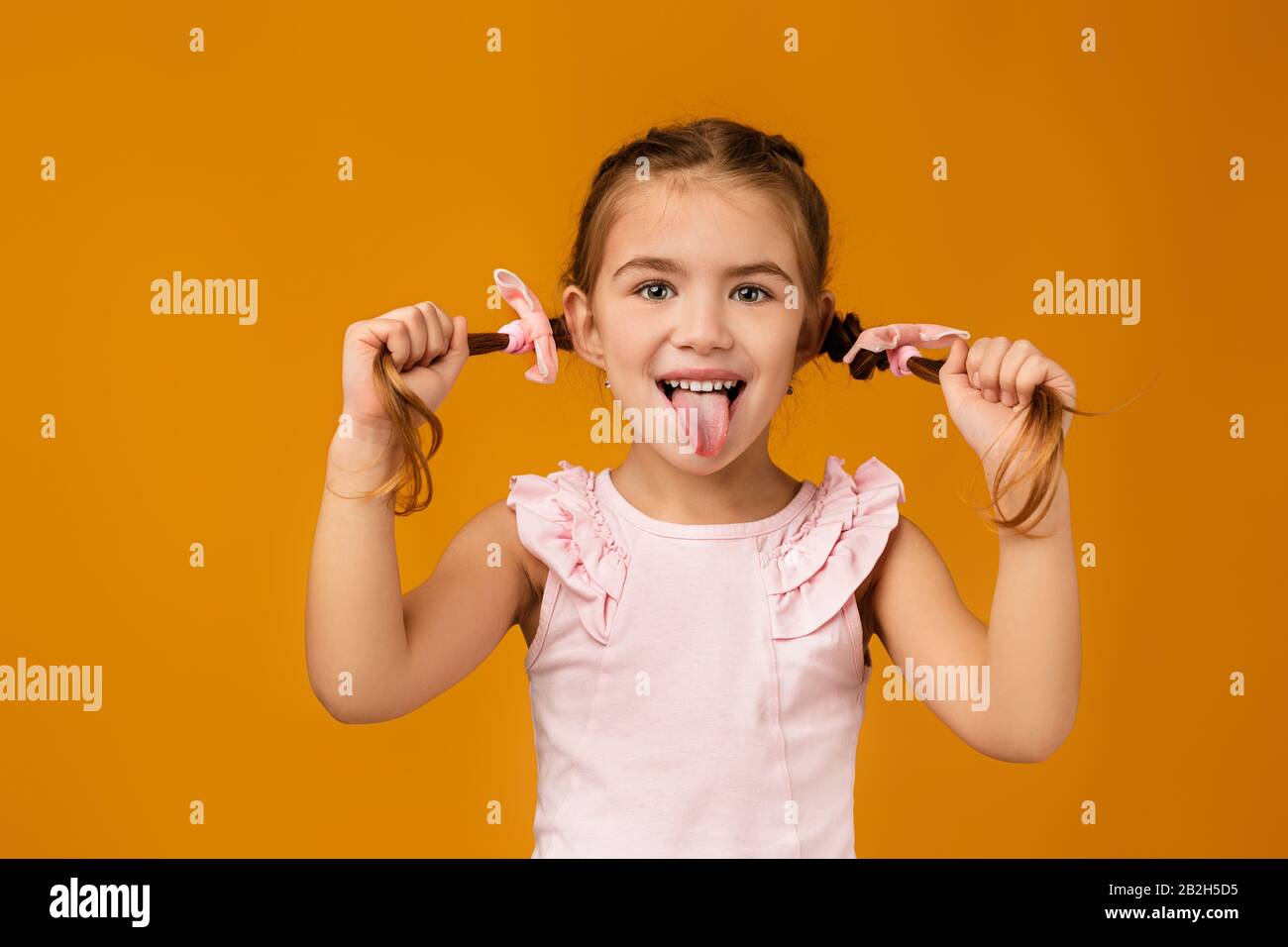 Fröhliches kleines Mädchen, das ihre Zunge auf gelbem Hintergrund zeigt. Gesichtsausdruck Stockfoto