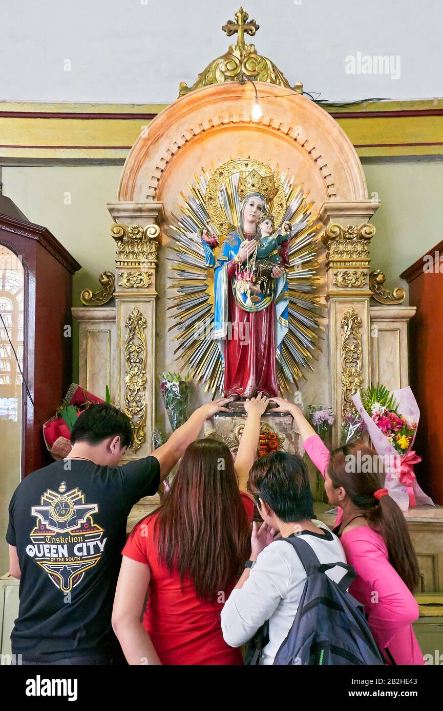 Manila, Philippinen: Eine Gruppe junger Filipinos verehren und berühren die Statue der Mutter Maria mit dem Jesuskind in der Quiapo-Kirche Stockfoto
