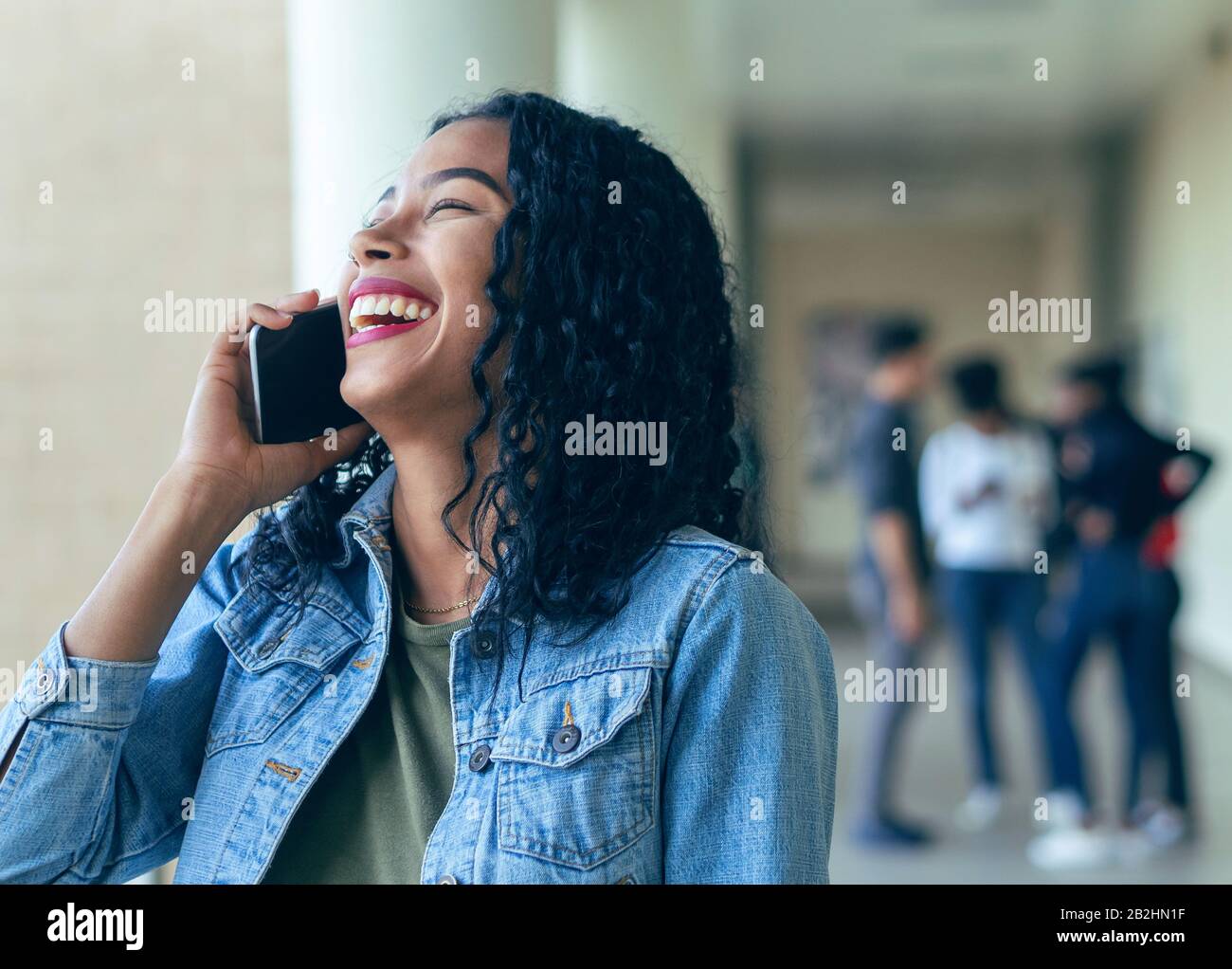 Ein College-Mädchen lacht mit einem Anruf mit ihren Klassenkameraden im Hintergrund Stockfoto